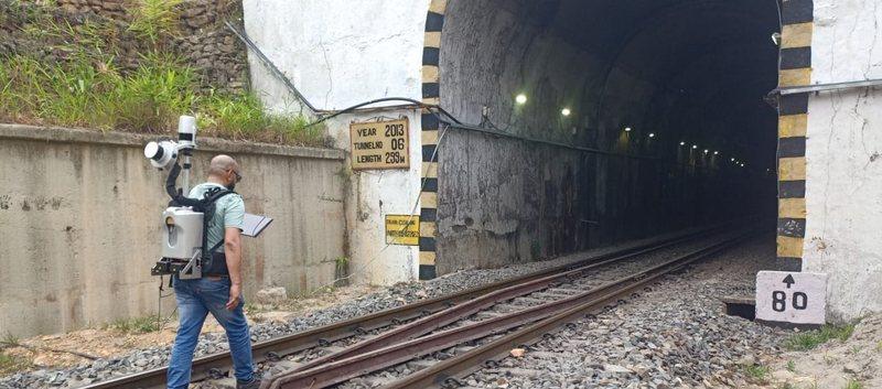 A surveyor carrying the backpack lidar unit walks along the ballast towards the mouth of a railway tunnel marked Tunnel No 06, length 299 m